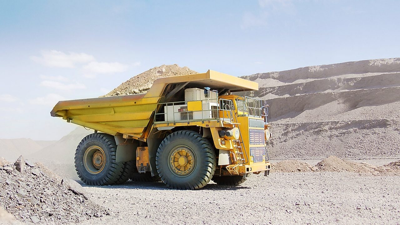 Yellow dumper truck driving through gravel